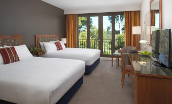 a hotel room with two beds , a window offering a view of trees , and a desk with a lamp at Yarra Valley Lodge, an EVT Hotel