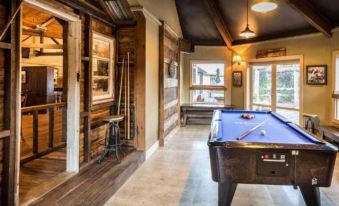 a billiards room with wooden walls , large windows , and an old pool table , accompanied by hanging lights and a window at Hanmer Springs Retreat