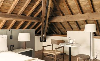 a cozy bedroom with a wooden ceiling and a bed , featuring a chair , a table , and lamps at August