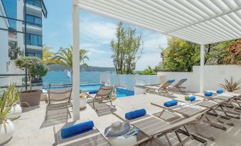 a large pool with lounge chairs and umbrellas is surrounded by a patio overlooking the water at Hotel Perla