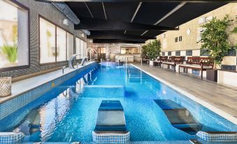 an indoor swimming pool with a diving board , surrounded by chairs and benches for seating at Salles Hotel Aeroport de Girona