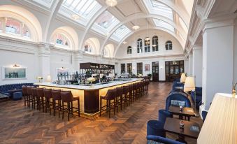 a modern bar area with a long wooden counter , several chairs , and a skylight overhead at Titanic Hotel Belfast