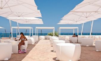 a woman in a bikini is sitting on a chair under umbrellas at an outdoor beach lounge area at Domina Zagarella Sicily