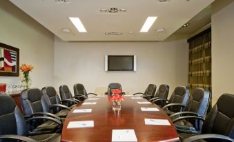 a conference room with a wooden table , black chairs , and papers on the table , as well as a television mounted on the wall at Novus Plaza Hodelpa