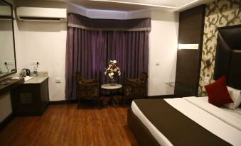 a modern hotel room with wooden flooring , white walls , and purple curtains , featuring a bed , chairs , table , and flowers at Hotel Shangri la