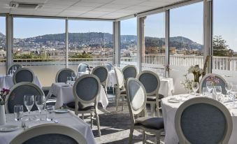 a dining room with white chairs and tables , set for a meal , overlooking a cityscape at Splendid Hotel & Spa Nice