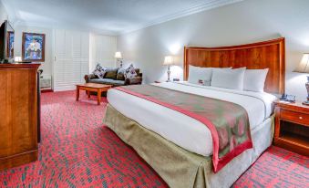 a large bed with a wooden headboard and footboard is in the center of a room with red carpeting at Ramada by Wyndham Metairie New Orleans Airport