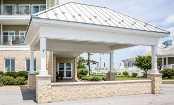 a white covered entrance to a building with a large white porch and columns , surrounded by trees and buildings in the background at Island Inn & Suites, Ascend Hotel Collection