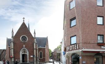 a brick building with a cross on top is next to a hotel and a small church at Hotel the Shepherd