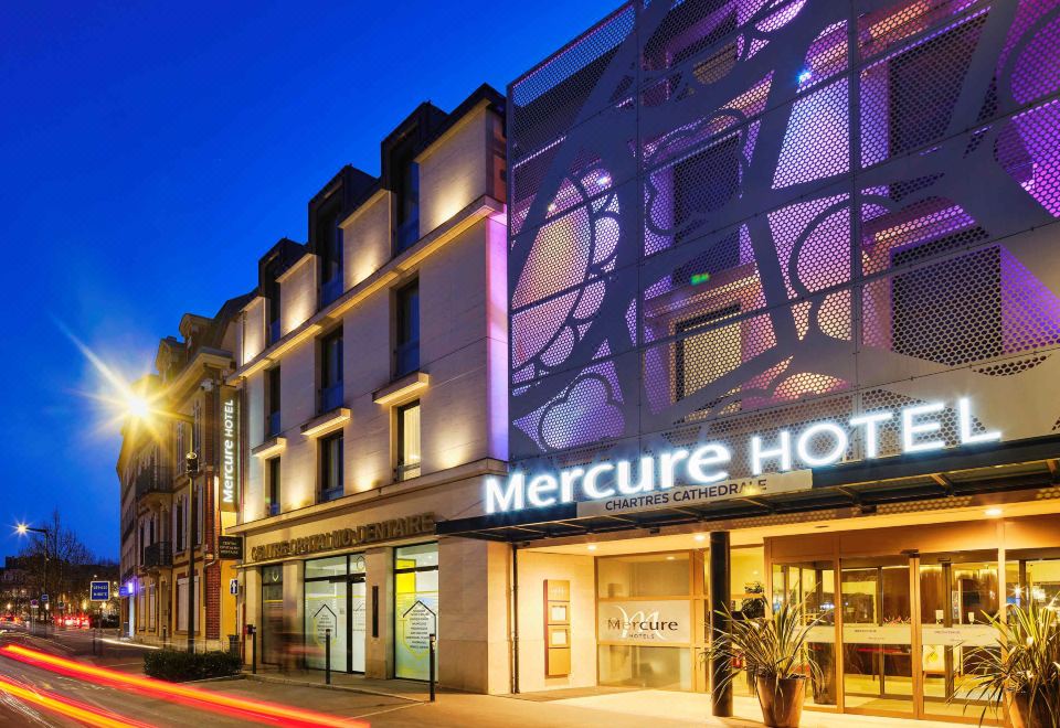 "a modern hotel building with the name "" mercure hotel "" displayed on its front , illuminated at night" at Mercure Chartres Cathedrale