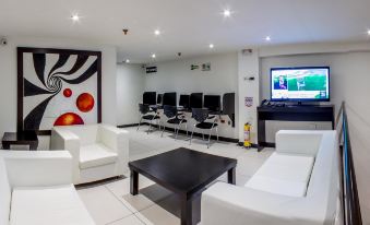 a modern living room with white couches , black coffee table , and a television displaying a soccer game at Hotel Metropolitano