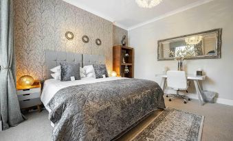 a large bed with a gray blanket is in a room with white walls and a chandelier at Carmel Apartments