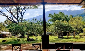 an outdoor dining area with a wooden table and chairs , surrounded by trees and mountains in the background at Jungle Hut