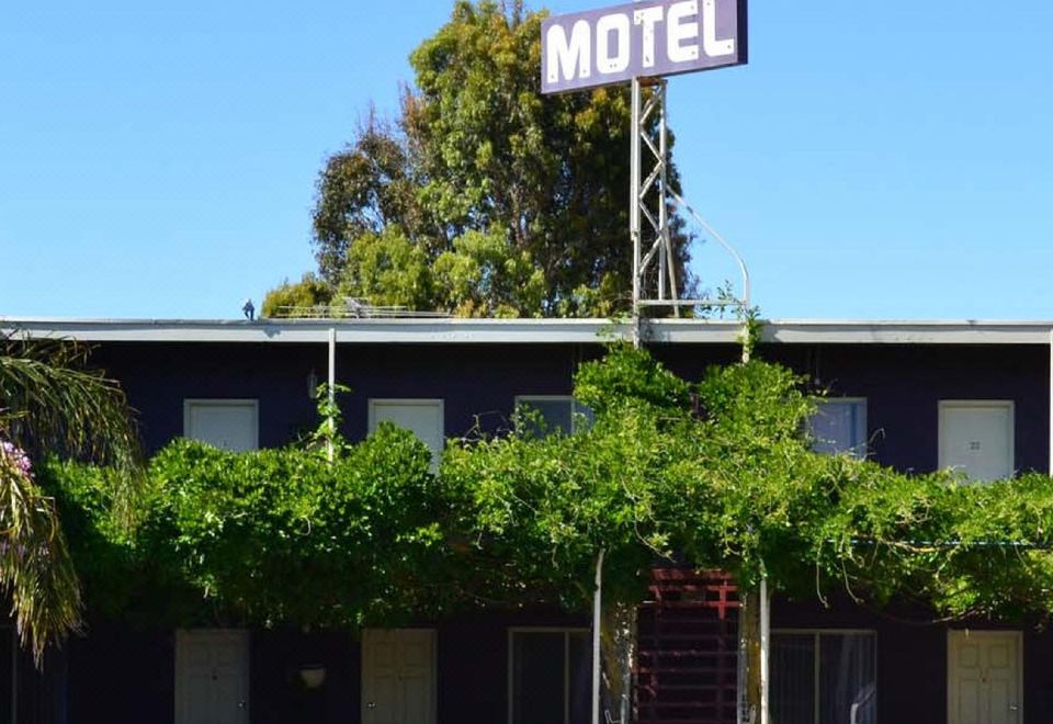 a black motel building with a sign , surrounded by trees and a clear blue sky at Barossa Gateway Motel
