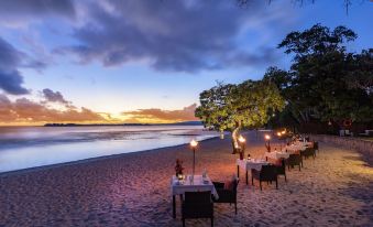 a beach scene with tables and chairs set up for dining , set against the backdrop of a beautiful sunset at Eratap Beach Resort