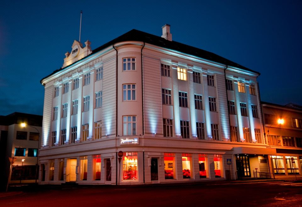 a large , white building with red and blue lights on the facade , lit up at night at Radisson Blu 1919 Hotel Reykjavik