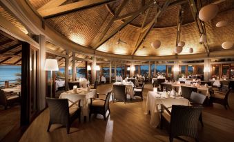 a large , well - lit restaurant with wooden floors and tables set for dining , featuring white tablecloths and chairs at Hilton Moorea Lagoon Resort and Spa