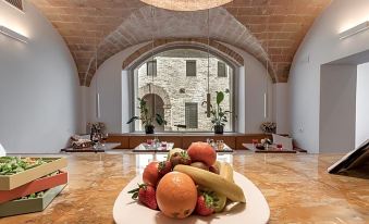 a large white plate filled with various fruits is placed on a marble floor in front of an arched window at Bosco Della Spina