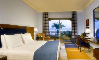 a modern hotel room with a large bed , white bedding , and a balcony offering views of the ocean at Kempinski Hotel Ishtar Dead Sea