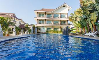 a large swimming pool is in front of a three - story building with palm trees and other plants surrounding it at Diamond Park Inn Chiangrai & Resort