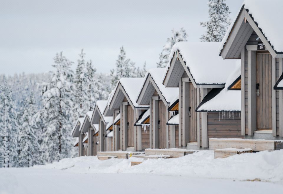 a row of wooden houses with snow on the roof is lined up in a snowy area at Northern Lights Village