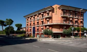 a red brick building with balconies , surrounded by trees and a street corner , under a clear blue sky at Best Western Cesena Hotel
