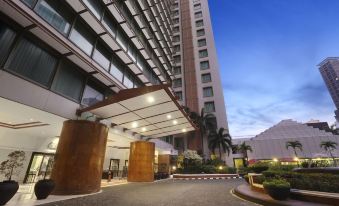 a modern hotel with a large glass building and a walkway leading up to it at Ascott Jakarta