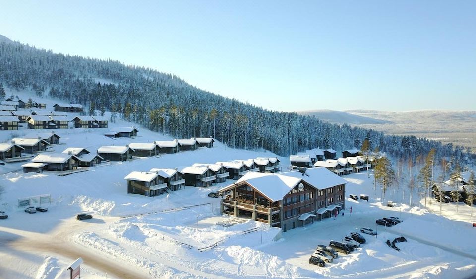 a snow - covered ski resort with multiple buildings , including a chalet - style house and several cabins , surrounded by trees at Mountain Lodge