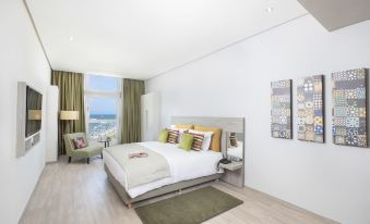 a large bed with white linens and green pillows is in a room with wooden floors , a window , and a chair at Marina Bay City Center