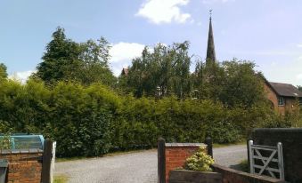 a gravel driveway leading up to a house with a church in the background , surrounded by trees at Church Farm Accomodation