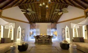a luxurious indoor dining area with a wooden ceiling , white walls , and a dining table surrounded by chairs at Dusit Thani Maldives
