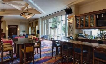 a large , well - lit room with multiple dining tables and chairs , as well as a bar area with stools at Marriott Dallas Las Colinas