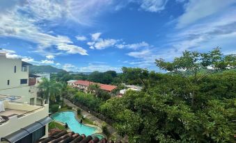 a view from a balcony , showcasing a tropical garden and a swimming pool with a view of the surrounding mountains under a blue sky dotted with clouds at Tropical Gardens