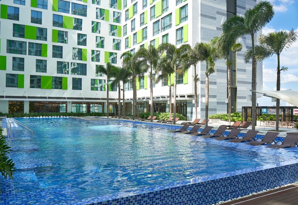 There is a spacious swimming pool in front of the building, accompanied by chairs and umbrellas on either side at Holiday Inn & Suites Saigon Airport