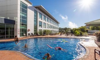 a group of people swimming in a large outdoor pool , surrounded by a hotel building at Rydges Rotorua, an EVT Hotel