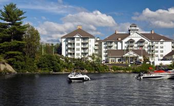 a large white building with multiple windows is situated on the shore of a lake at Residence Inn Gravenhurst Muskoka Wharf