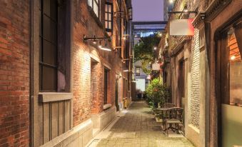 At night, a narrow city alley is lined with shops on both sides, and a person walks through it with an umbrella at Greentree Inn (Shanghai Jingan)