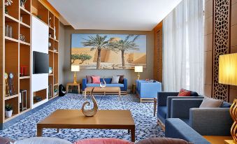 a modern living room with a large painting on the wall , multiple couches , and chairs arranged around a coffee table at Hilton Garden Inn Tabuk