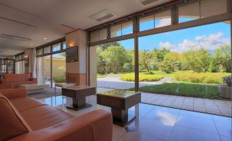 a spacious living room with large windows overlooking a garden and mountains , creating a serene atmosphere at Fuji Matsuzono Hotel