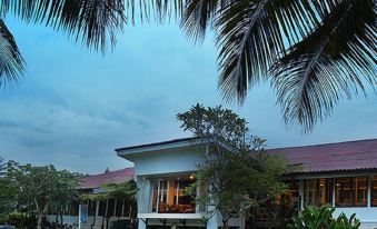 a large house with a red roof is surrounded by palm trees and grass , under a cloudy sky at Asana Biak Papua Hotel