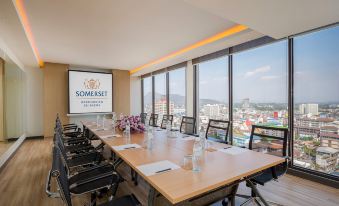 a conference room with a large table , chairs , and a view of the city through large windows at Somerset Harbourview Sri Racha