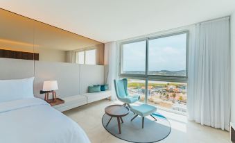 a modern hotel room with a large window overlooking the city , featuring a bed , chair , and small table at Radisson Blu Aruba
