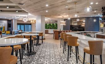 a modern restaurant with wooden tables and chairs , a bar , and a tv in the background at Cambria Hotel Detroit-Shelby Township