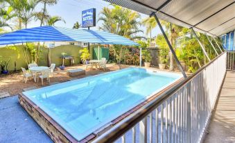 a swimming pool with a blue and white striped umbrella on the side , surrounded by palm trees and a wooden deck at Blue Shades Motel