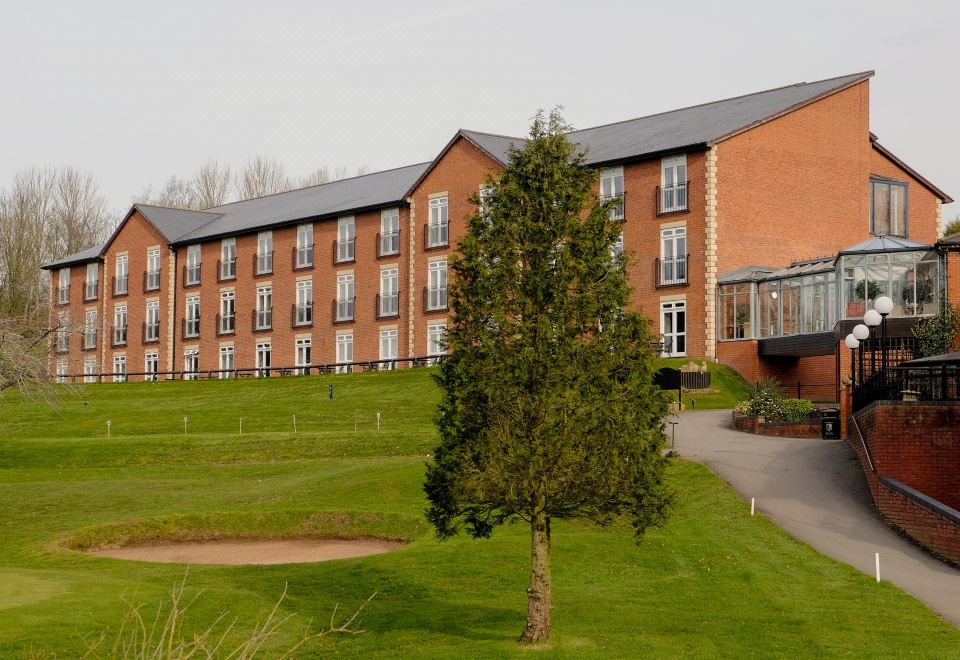 a large brick building surrounded by a grassy field , with a golf course in the foreground at Macdonald Hill Valley Hotel Golf & Spa