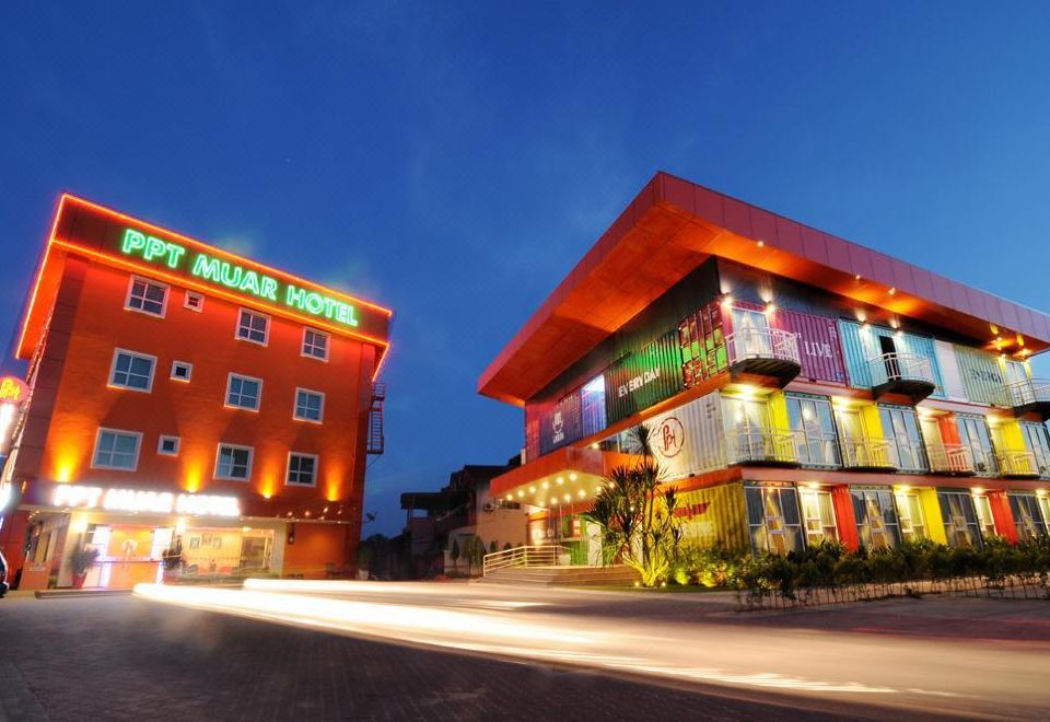 a brightly lit hotel with a red exterior , situated on a street at night with lights from the nearby buildings at Ppt Muar Hotel