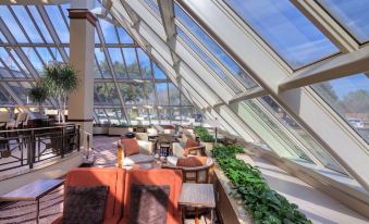 a large , modern room with multiple seating arrangements and a bar area under a large glass roof at Hilton Houston Westchase