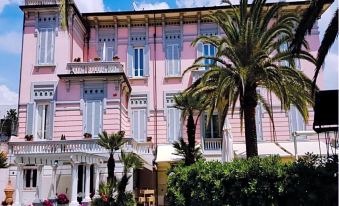 a pink building with white shutters and a palm tree in front of it , surrounded by greenery at Hotel Europa