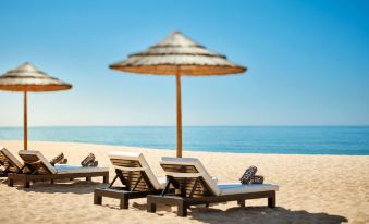 a row of sun loungers and a straw umbrella are set up on a sandy beach near the ocean at Tivoli Marina Vilamoura