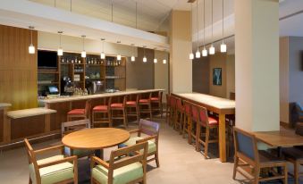 a well - lit restaurant with wooden tables and chairs , a bar area , and hanging lights overhead at Hyatt Place Denver Cherry Creek